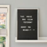 Eine Frau arbeitet lächelnd an einem hellen, gut ausgestatteten Home-Office-Arbeitsplatz mit Pflanzen und Tageslicht.