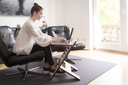 Person sitzt ergonomisch an einem höhenverstellbaren Schreibtisch mit Bürostuhl, Monitor auf Augenhöhe und geordnetem Arbeitsplatz.