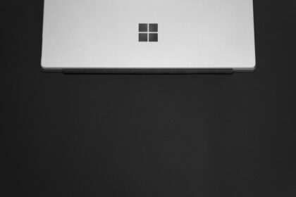 Ein schwarzes Microsoft Surface Dock 2 mit angeschlossenen Kabeln für Monitore und Peripherie auf einem aufgeräumten Schreibtisch.